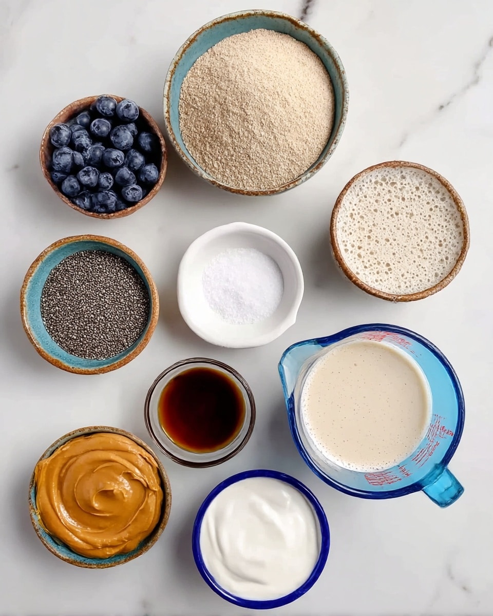 This image shows nine small bowls and a glass measuring cup arranged on a white marbled surface. The bowls contain different ingredients: one bowl is filled with dark blue blueberries, another with a light brown powder that looks like yeast, and a larger bowl filled with tiny black chia seeds. A small white dish holds white salt, while another has a dark amber liquid, possibly vanilla extract, next to a smaller bowl holding a similar dark syrup. One bowl contains smooth peanut butter with a light brown color, and another holds thick white yogurt inside a bowl with a blue rim. The glass measuring cup is filled with a frothy light beige liquid. All the bowls are round, mostly ceramic, and the colors mostly earthy tones except the yogurt bowl with a blue rim. photo taken with an iphone --ar 4:5 --v 7