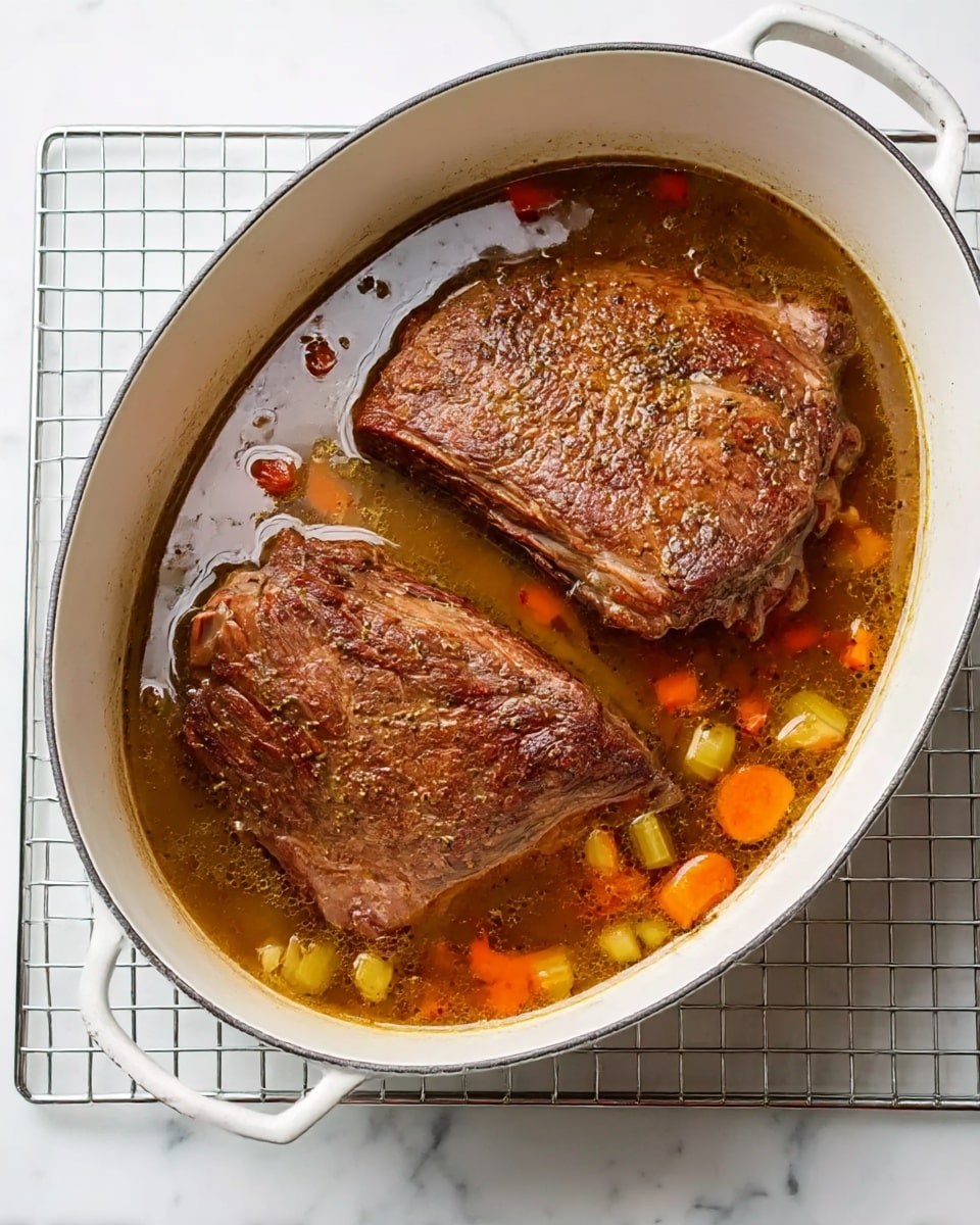 The image shows a white oval pot filled with two large pieces of browned roast beef resting in a clear brown broth with small pieces of orange carrot and green celery scattered around. The pot sits on a silver wire rack over a white marbled surface. The beef has a slightly rough texture with a seared crust, and the broth looks light but flavorful with bits of vegetables floating inside. Photo taken with an iphone --ar 4:5 --v 7