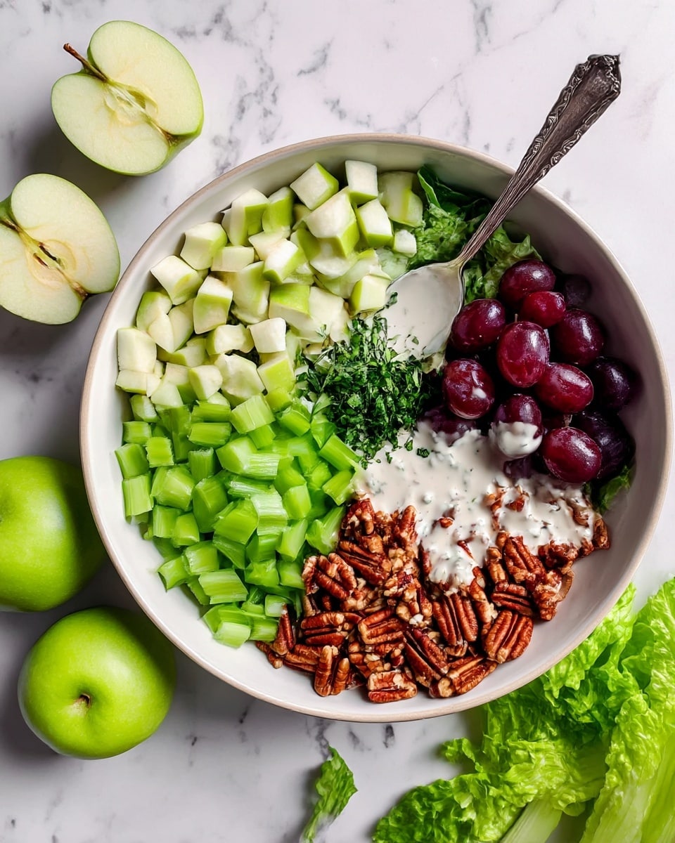 A white bowl holds a fresh salad arranged in five distinct sections on a white marbled surface. Starting from the top left, there are pale green apple cubes with skins, next to bright green chopped celery on the bottom left. In the center is a small pile of chopped dark green herbs. The top right features halved dark purple grapes with a silver spoon resting on this side. The bottom right has roughly chopped brown pecans. A creamy white dressing is drizzled unevenly over all the ingredients. Nearby, there are two whole green apples and some fresh loose green lettuce leaves. Photo taken with an iphone --ar 4:5 --v 7