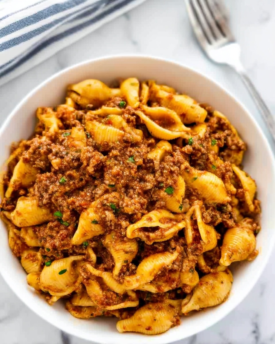A close-up of a spoon full of pasta shells stuffed with minced meat in a creamy orange sauce sprinkled with small green herbs. The pasta shells are tightly packed and have a smooth, shiny texture, with the creamy sauce clinging to them. The background shows more of the same pasta dish, with a rich, creamy, orange-colored sauce and visible bits of meat. The spoon is held by a woman's hand above a white marbled surface. The whole image has warm, bright colors and sharp focus on the pasta. photo taken with an iphone --ar 4:5 --v 7