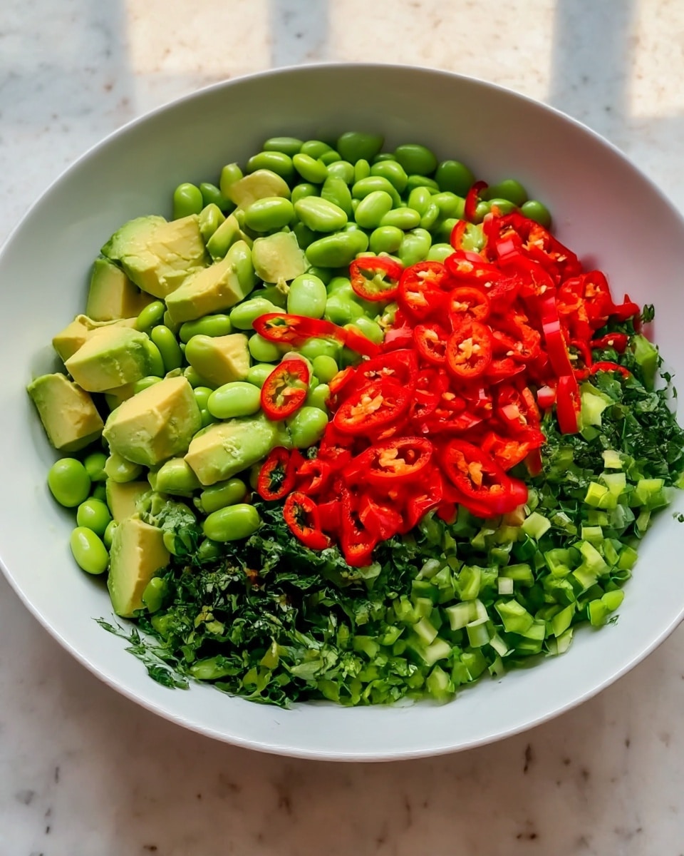 A white bowl filled with five distinct layers of fresh ingredients arranged side by side. Starting from the left, there are chunks of light green avocado with a smooth texture, next to a heap of shiny, light green edamame beans. In the middle, a bright red layer of thinly sliced chili peppers adds a pop of color and texture. To the right of the chili peppers, finely chopped dark green herbs fill the space, next to a section of small, vibrant green diced vegetables. The bowl is placed on a white marbled surface, with natural lighting highlighting the fresh colors. photo taken with an iphone --ar 4:5 --v 7