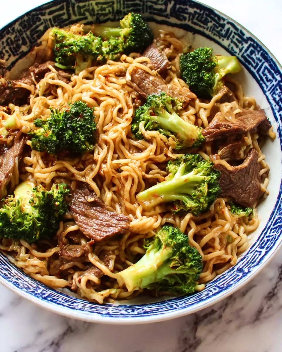The image shows a white bowl decorated with blue patterns, filled with cooked noodles mixed with pieces of broccoli and sliced cooked beef. The noodles are light brown and look slightly glossy from the sauce. The broccoli pieces are bright green with a soft texture, and the beef slices are dark brown, tender and juicy. The bowl sits on a white marbled surface. Photo taken with an iphone --ar 4:5 --v 7