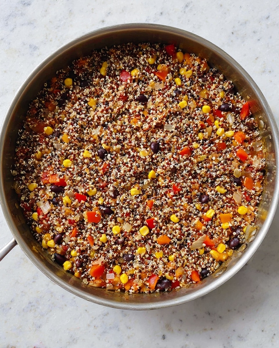 A silver pan holds a colorful cooked dish with two clear layers visible. The bottom layer is a mix of small, chopped vegetables including bright yellow corn, red bell pepper pieces, black beans, and translucent onions, creating a vibrant base. On top, there is a thick layer of cooked quinoa with a mix of white, red, and black grains, giving a textured, speckled look. The pan is placed on a surface with white marbled texture, and the food looks warm and well combined. photo taken with an iphone --ar 4:5 --v 7