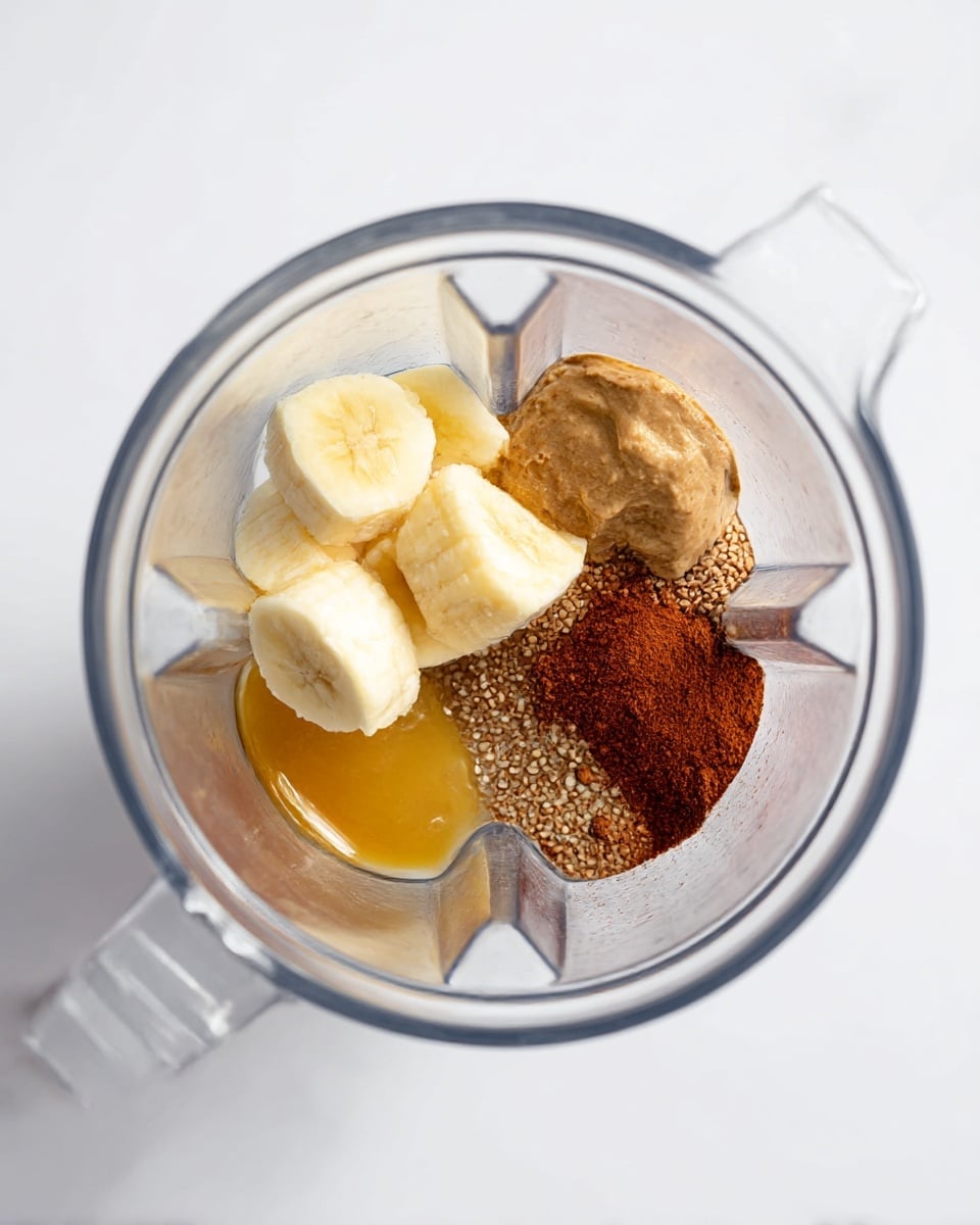 Inside a clear blender, there are several ingredients placed together: three chunky pieces of frozen light yellow banana on the left, a small pool of shiny golden honey at the bottom left, a mound of light brown creamy almond butter on the top right, a heap of dark brown ground flax seeds in the center, and a patch of reddish-brown cinnamon powder on the bottom right. The blender sits on a white marbled surface. photo taken with an iphone --ar 4:5 --v 7