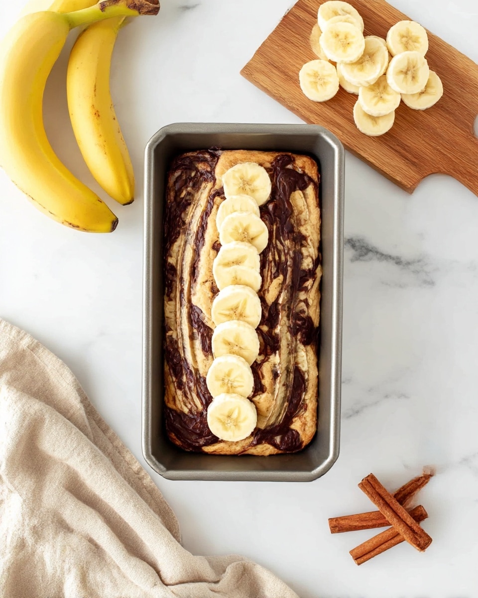 A loaf pan filled with light beige banana bread batter has dark brown swirls of chocolate spread across the top layer. On top, a row of six evenly spaced banana slices, pale yellow with light cream centers, runs down the middle. To the left, three whole yellow bananas lie on a white marbled surface, and to the right, a small wooden board holds a neat pile of more banana slices. In the lower right corner, three brown cinnamon sticks lay side by side, and a light beige cloth is draped softly in the lower left corner. photo taken with an iphone --ar 4:5 --v 7