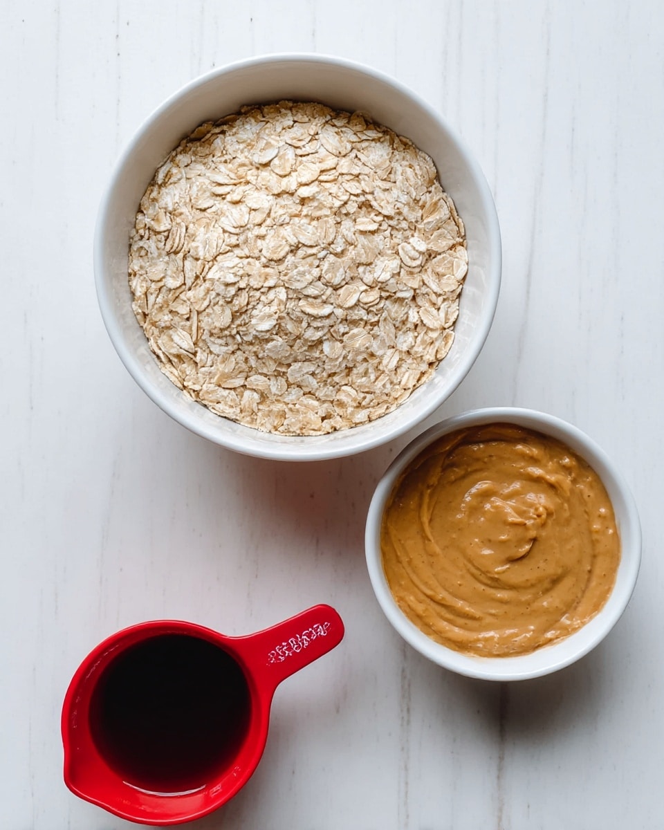 The image shows three containers with ingredients on a white marbled surface. At the top, a white bowl is filled with light beige rolled oats, with a dry and flaky texture, filling the bowl to the top. Below the bowl, on the right side, there is a white bowl filled with smooth, creamy peanut butter in a light brown color. On the left side, next to the peanut butter, there is a small red measuring cup holding a dark brown liquid, likely syrup. The containers are arranged closely together with a clean, bright background. photo taken with an iphone --ar 4:5 --v 7