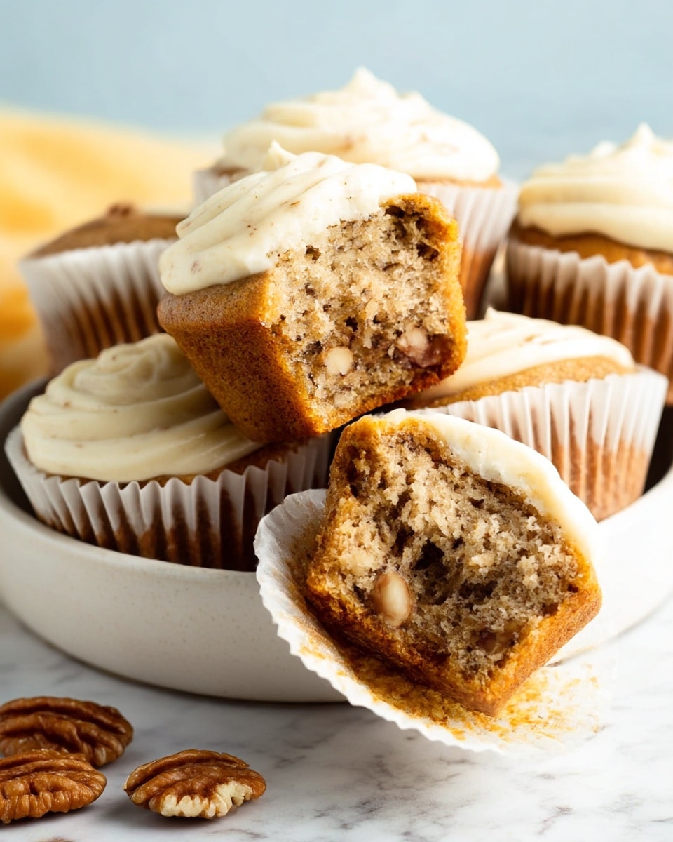 A close-up shows five muffins in white paper cups inside a white bowl on a white marbled surface. The muffins have two layers: the bottom layer is a light brown, softly textured cake with small dark specks, and the top layer is creamy white frosting swirled with light brown spots. One muffin is lifted, showing a bite taken out, revealing a soft, moist inside with visible small nut pieces. A few whole nuts lie scattered near the bowl outside. Photo taken with an iphone --ar 4:5 --v 7