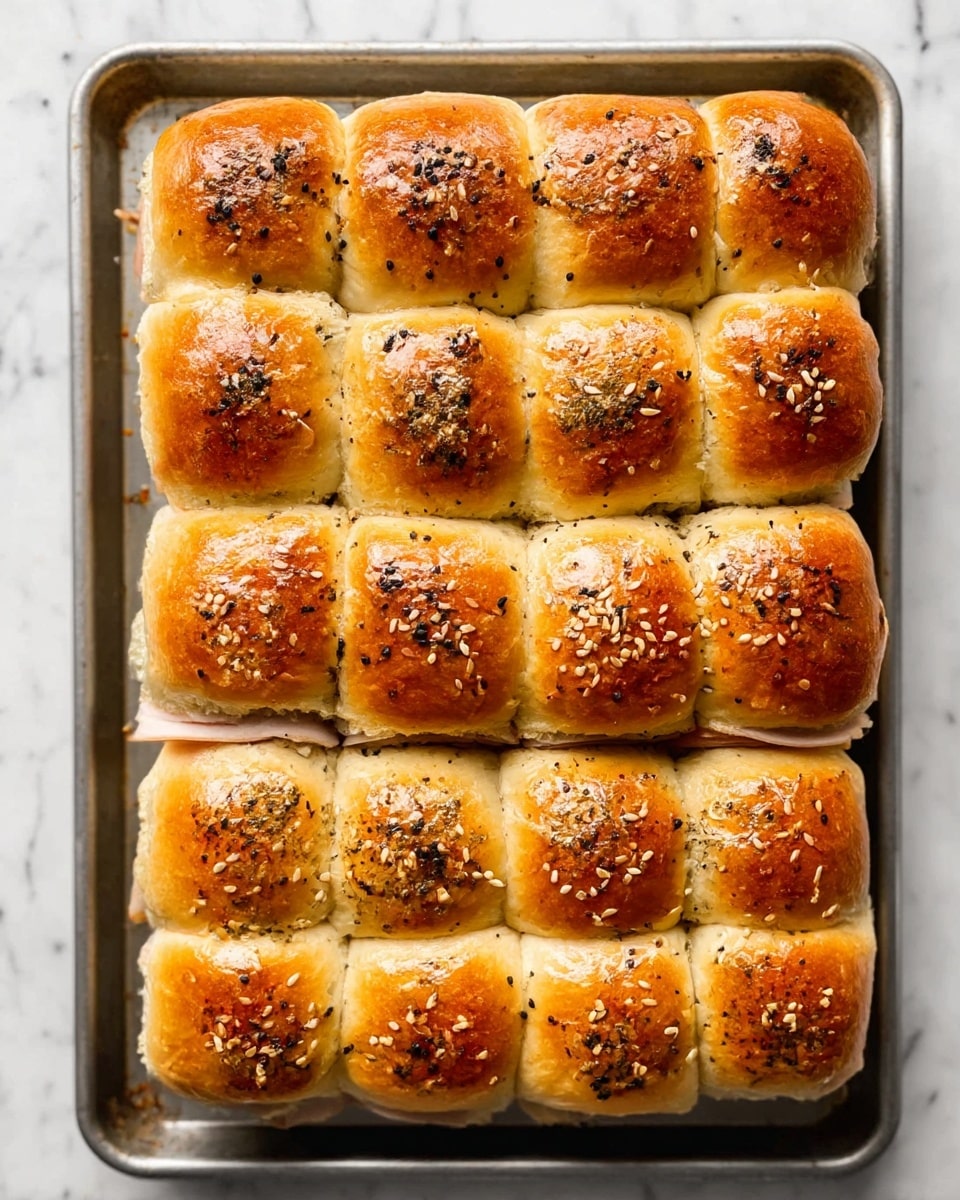 A tray holds a square sandwich made of twelve golden brown dinner rolls arranged in a 3x4 grid, each roll topped with sesame seeds and black pepper flakes. The rolls have a shiny, slightly crispy surface. Between the layers of the soft, fluffy rolls, thin slices of light beige turkey meat can be seen peeking out around the edges. The tray rests on a white marbled surface, and the sandwich looks freshly baked and neatly connected at the sides. photo taken with an iphone --ar 4:5 --v 7
