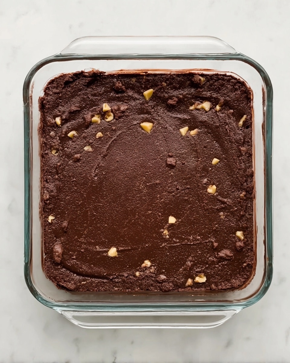 The image shows four clear glass bowls on a white marbled surface. The largest bowl at the left holds many small dark brown chocolate chips tightly packed together. To the right of it are two smaller bowls: the one at the top contains a light creamy yellow liquid, while the one below has light brown chopped nuts. Below the large bowl, there is a small bowl with white butter cubes. The bowls are neatly arranged with some space between them. photo taken with an iphone --ar 4:5 --v 7