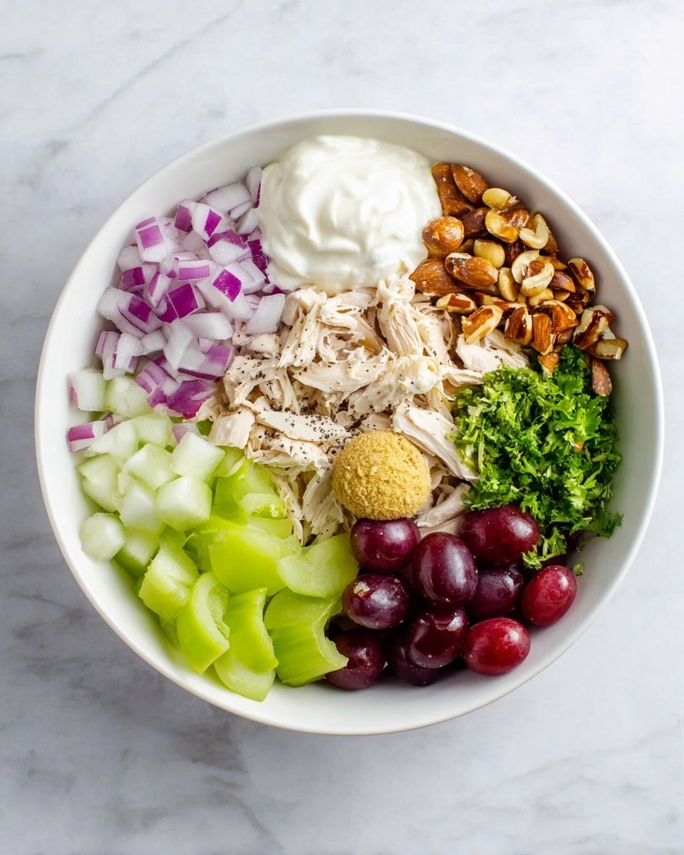 A white bowl sits on a white marbled surface filled with seven distinct layers arranged side by side. Starting at the top left is a pile of chopped purple and white onions with a crisp texture. Next to it on the right are chopped brown almonds with a rough texture. Below the almonds is a portion of shredded pale beige chicken sprinkled with black pepper. To the bottom right of the chicken is a small heap of bright green chopped parsley. Below the parsley are dark red grapes, some whole and some sliced in half showing their juicy inside. On the bottom left is a pile of sliced green celery sticks. Above the celery and to the left center is a dollop of smooth white yogurt. Finally, at the center of the bowl is a round scoop of grainy yellow mustard. Photo taken with an iphone --ar 4:5 --v 7