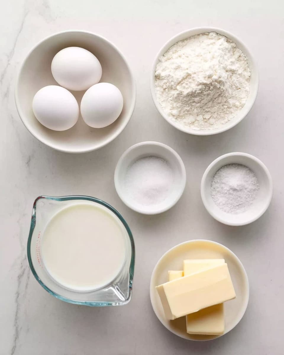 The image shows six small white bowls and a clear glass measuring cup arranged on a white marbled surface. One white bowl holds four white eggs, another contains white flour with a slightly rough texture on the edges. A third bowl has granulated white sugar, and a fourth one has a small amount of salt with a grainy texture. The small white bowl in the front center has two rectangular blocks of pale yellow butter. The clear glass measuring cup on the left is filled with a smooth white liquid, likely milk. The items are spread evenly with a clean and simple look photo taken with an iphone --ar 4:5 --v 7