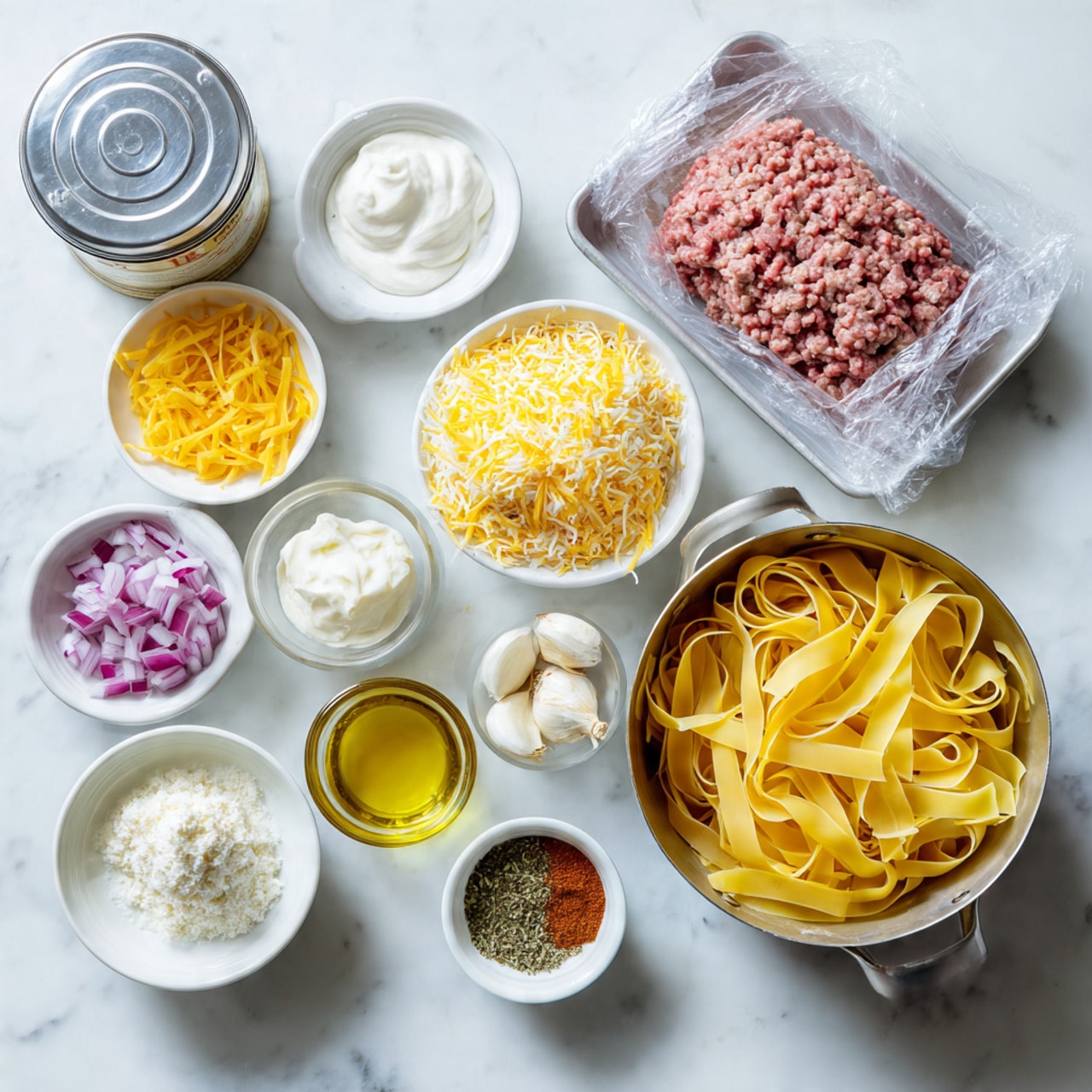 The image shows a group of ingredients arranged neatly on a white marbled surface with soft shadows. There is a tray of raw ground meat wrapped in clear plastic near the top right. Below it, a white bowl filled with finely shredded yellow and orange cheese sits. Next to the cheese bowl, a metal pot full of uncooked wide yellow pasta ribbons is placed. Scattered around are smaller white bowls containing diced red onions, a few cloves of garlic, olive oil, sour cream, and a spreadable white cheese. A small white plate holds a mix of dry seasonings including pepper and herbs, and a glass cup contains a reddish-brown powdered spice. A small container of salt is nearby, and a closed silver tin can is on the top left. The whole setting is lit well, focusing on the colorful ingredients, photo taken with an iphone --ar 4:5 --v 7