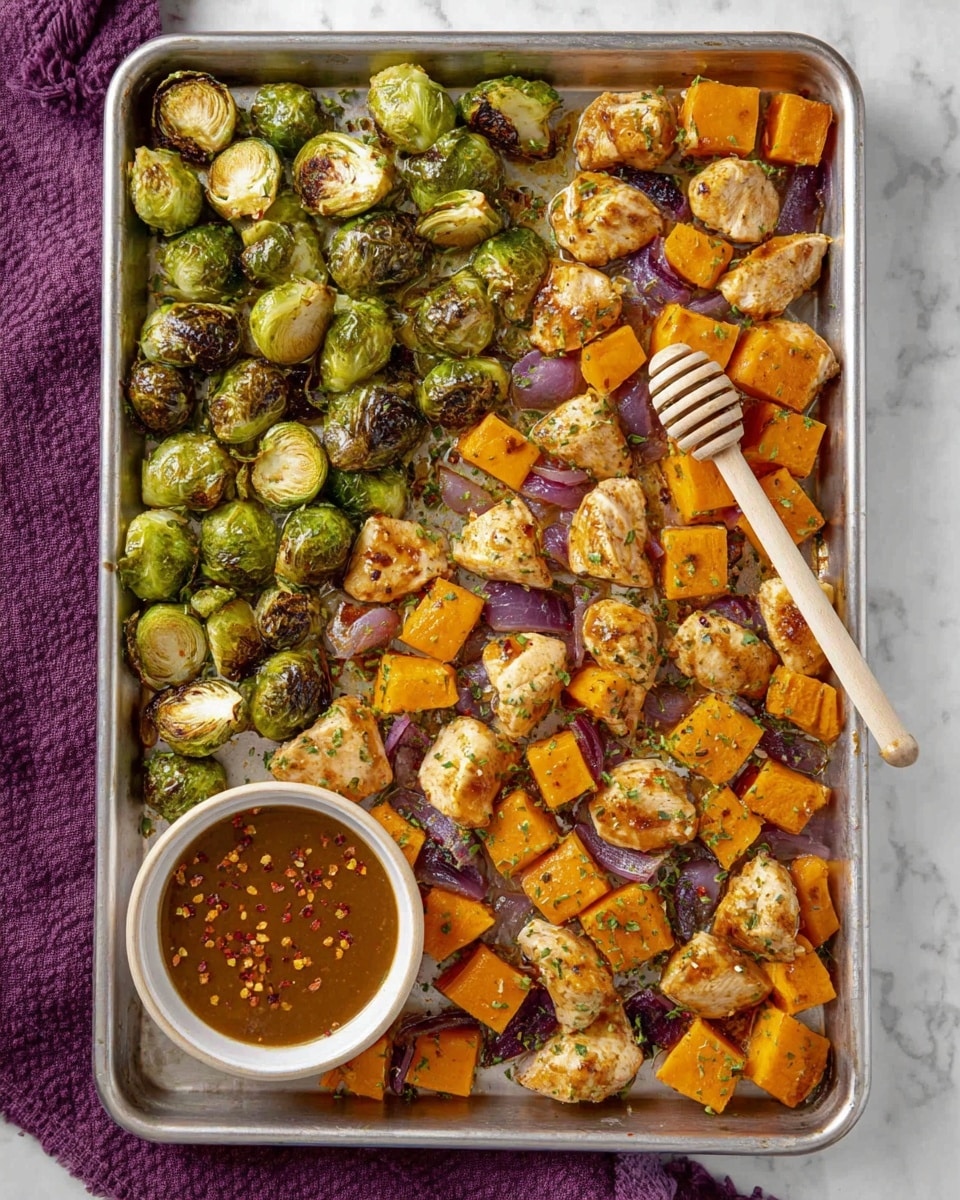 The image shows a large metal baking tray filled with three main layers of roasted food. The first layer consists of small green Brussels sprouts, some showing charred spots. The second layer has orange sweet potato cubes, evenly roasted with slightly browned edges. The third layer is made up of small pieces of cooked chicken, golden brown with herbs sprinkled on top. Scattered thin pieces of sautéed red onion add a touch of purple among the other items. A small white bowl filled with a brown sauce, topped with red pepper flakes and a light wooden honey dipper inside, is placed near the top right on the tray. The whole scene is set on a white marbled surface with a purple fabric partially visible at the bottom left. Photo taken with an iphone --ar 4:5 --v 7