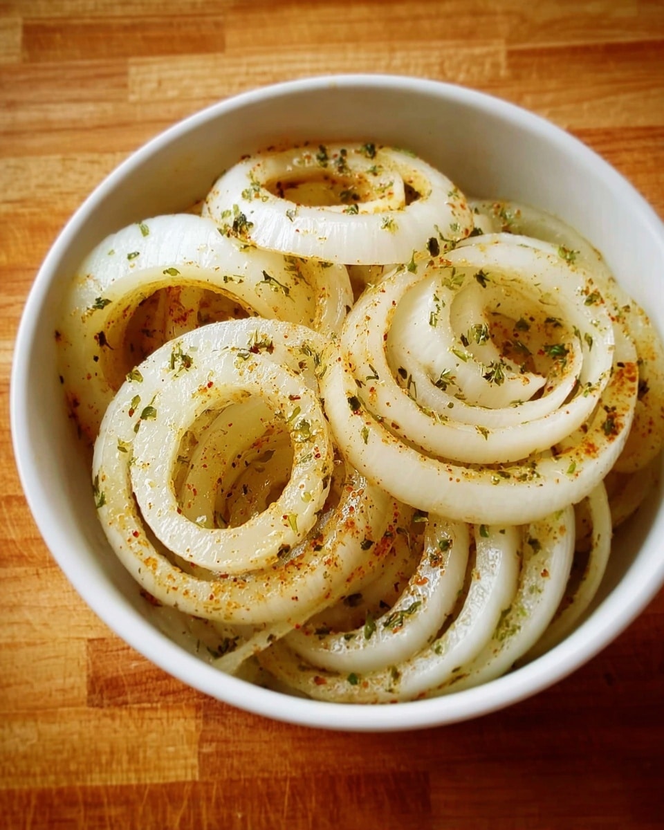A white bowl filled with several rings of sliced onions, each ring having a pale yellow and white color with a slightly translucent texture. The onion rings are sprinkled with a light coating of green herbs and small bits of spices evenly spread across the layers. The bowl is placed on a wooden surface, showing warm brown tones and a natural wood grain pattern. photo taken with an iphone --ar 4:5 --v 7