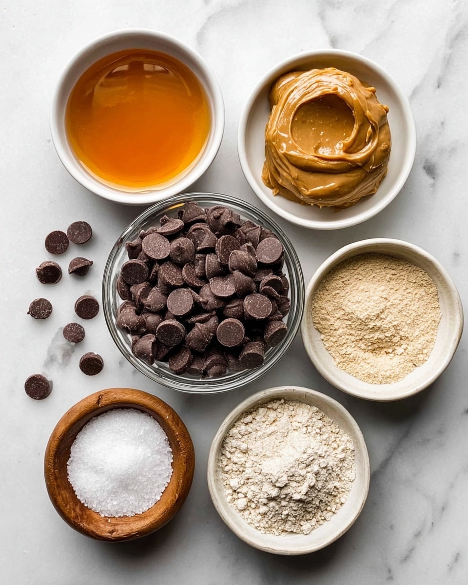The image shows six small bowls arranged on a white marbled surface, each containing a different ingredient. In the center, there is a clear bowl full of dark chocolate chips that are round and smooth. To the top right, a clear bowl holds a creamy peanut butter with a smooth, slightly shiny surface. At the top left, a white bowl contains golden amber-colored liquid syrup with a reflective surface. At the bottom right, a white bowl is filled with light beige powder that looks dry and crumbly. On the bottom left, there is a small wooden bowl with coarse white salt grains, while above it, a small white bowl has a white, solid scoop of coconut oil with a soft texture. Around the bowls, a few chocolate chips are scattered on the surface. The photo was taken with an iphone --ar 4:5 --v 7