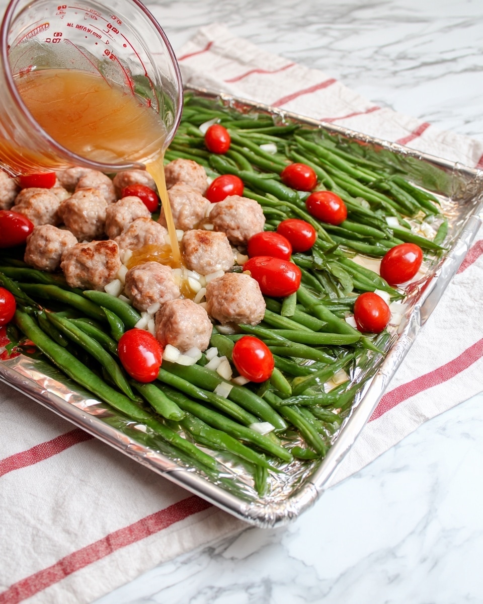 The image shows a baking tray lined with foil, placed on a white marbled surface with a striped cloth under it. On the tray, there is a base layer of fresh green beans spread out evenly. Scattered over the green beans are whole red cherry tomatoes and small round raw meatballs in a light pink color. Above the tray, a transparent glass measuring cup is tilted, pouring a light brown sauce with small white chopped pieces into it, likely garlic. The overall look is fresh and colorful with the green beans, bright red tomatoes, and pale meatballs. Photo taken with an iphone --ar 4:5 --v 7