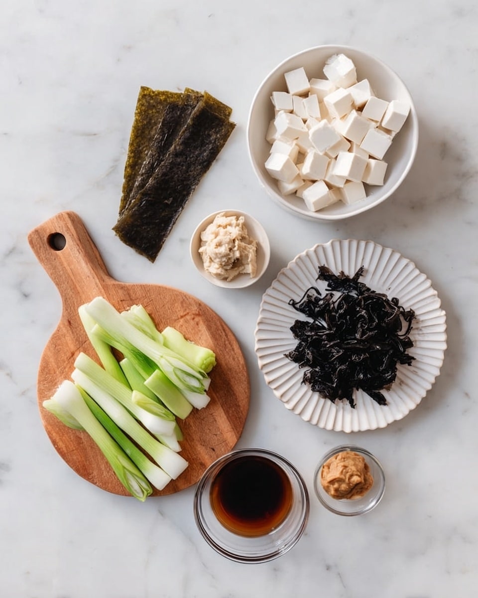 The image shows six ingredients on a white marbled surface. At the top center, there is a white bowl filled with small white tofu cubes. To the left, there is a piece of dark brown dried seaweed lying flat. Below the seaweed, a wooden round board with a handle holds sliced light green spring onions. To the right of the spring onions, there is a white fluted plate containing black dried seaweed pieces. Below this plate, a small white bowl contains a pale brown paste. At the bottom center, there is a small clear glass bowl with a dark brown liquid. Photo taken with an iphone --ar 4:5 --v 7