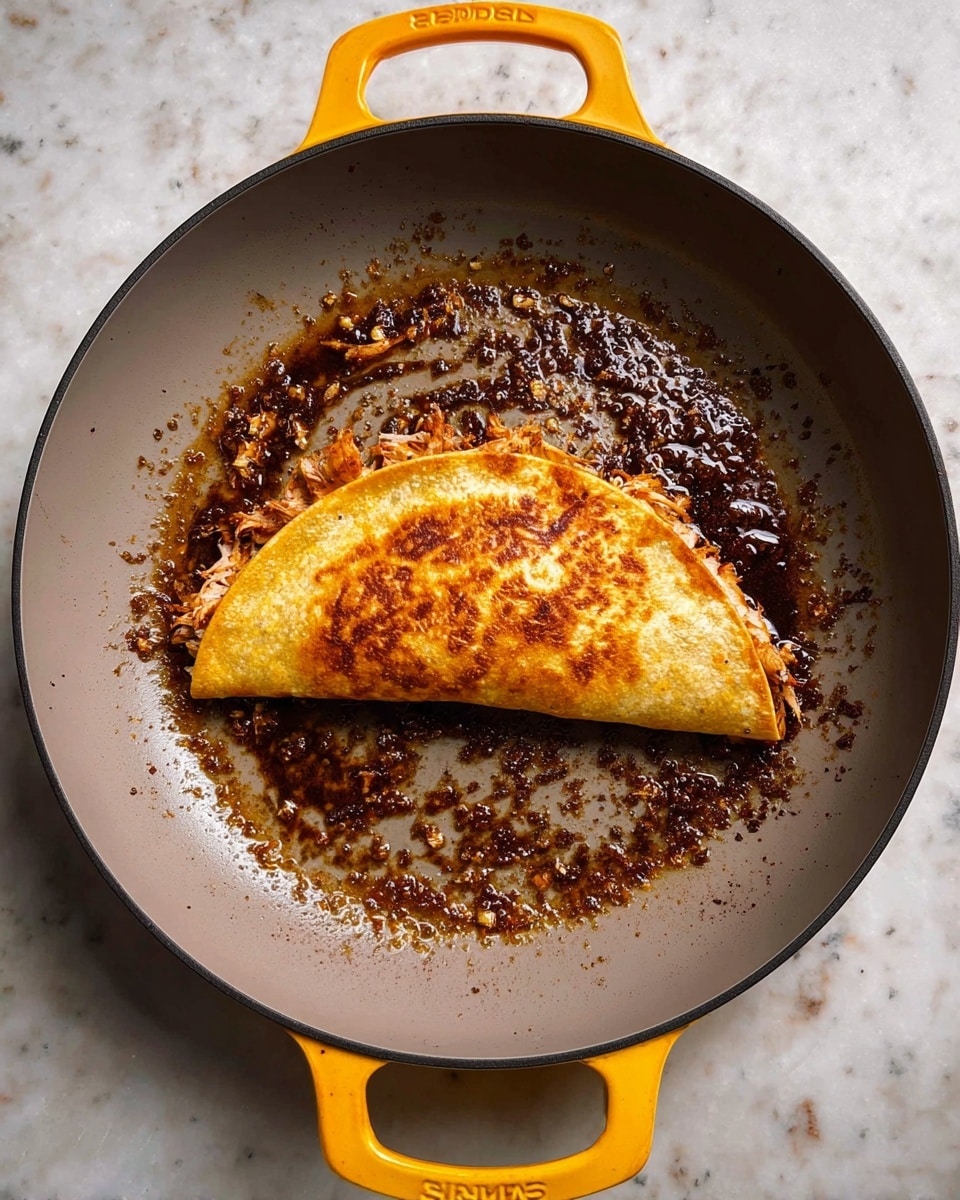 A golden brown folded taco sits in the center of a grey pan with bright yellow handles, surrounded by dark brown crispy bits and oil glistening around the edges. The taco's surface is evenly browned with a slightly crispy texture, and inside, tender shredded portions peek out. The pan's light grey interior contrasts with the rich colors of the taco and the oil. The background is a white marbled texture. photo taken with an iphone --ar 4:5 --v 7