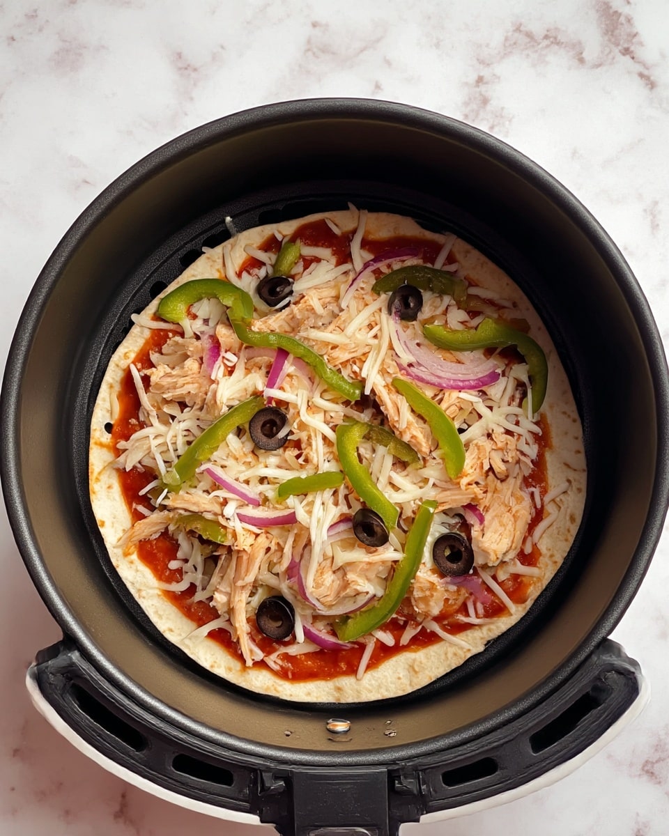 A small pizza with one visible layer of thin tortilla as the base inside a round black air fryer basket is shown. On top of the tortilla is a spread of red tomato sauce covering most of the surface. Over the sauce is a layer of shredded white cheese evenly scattered. Pieces of light beige cooked chicken are spread sparsely on the cheese. Thin slices of purple onion and rings of black olives are mixed with green bell pepper strips on top, creating a colorful and fresh look. The basket sits on a surface with a white marbled texture. Photo taken with an iphone --ar 4:5 --v 7