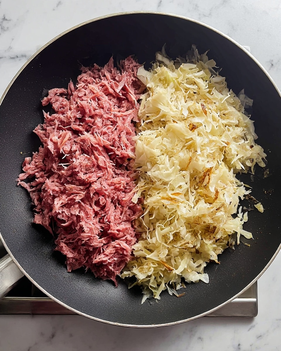 In a large black frying pan, two main layers sit side by side: on the left, a pile of finely shredded pinkish-red meat with a soft and slightly crumbly texture; on the right, a heap of light yellow and white browned shredded cabbage with slightly crispy edges. The frying pan rests on a stovetop with a metal front edge visible beneath. The whole scene is set on a white marbled surface. photo taken with an iphone --ar 4:5 --v 7