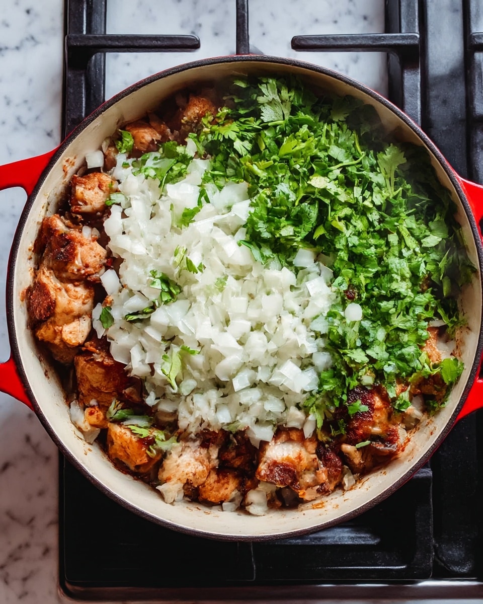 A top view of a round white pot with red handles, filled with browned chicken pieces as the bottom layer. Over the chicken, there is a thick layer of chopped white onions and fresh green cilantro leaves scattered evenly. The pot sits on a black stove, with some steam rising from the food, showing it is hot and cooking. The background is a white marbled surface photo taken with an iphone --ar 4:5 --v 7