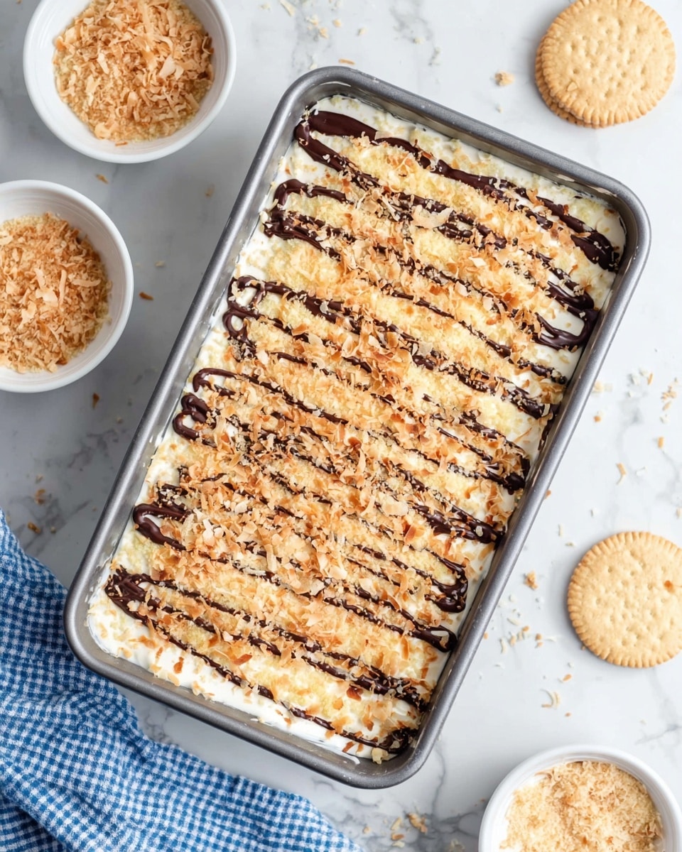 A rectangular metal baking pan holds a dessert with multiple layers. The bottom layer is creamy white, smooth and thick. On top of this, there is a crumbly pale yellow layer, likely some kind of crust or streusel. Toasted coconut flakes with a golden-brown color cover the surface evenly, adding texture. Thin dark chocolate drizzle lines run diagonally across the dessert, contrasting with the light layers. Around the pan on the white marbled surface are small white bowls with extra toasted coconut and crumbs. Two round light beige butter cookies are placed near the top right corner. A blue and white checked cloth is partly visible at the bottom left. Photo taken with an iphone --ar 4:5 --v 7