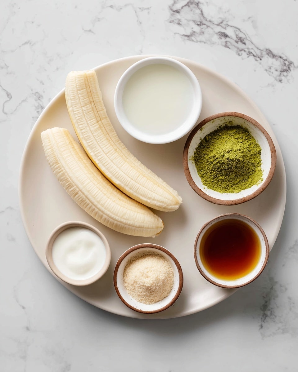 A white plate sits on a white marbled surface holding two peeled ripe bananas with a smooth, pale yellow color. Around it are four small brown-rimmed bowls; one filled with bright green matcha powder with a fine, powdery texture, another with creamy white coconut milk that has a smooth and shiny surface, a third containing light beige monkfruit powder in a powdery form, and the last holding dark amber vanilla extract with a transparent liquid texture. A small white bowl with clear hot water is also placed near the group, completing the arrangement. The photo taken with an iphone --ar 4:5 --v 7