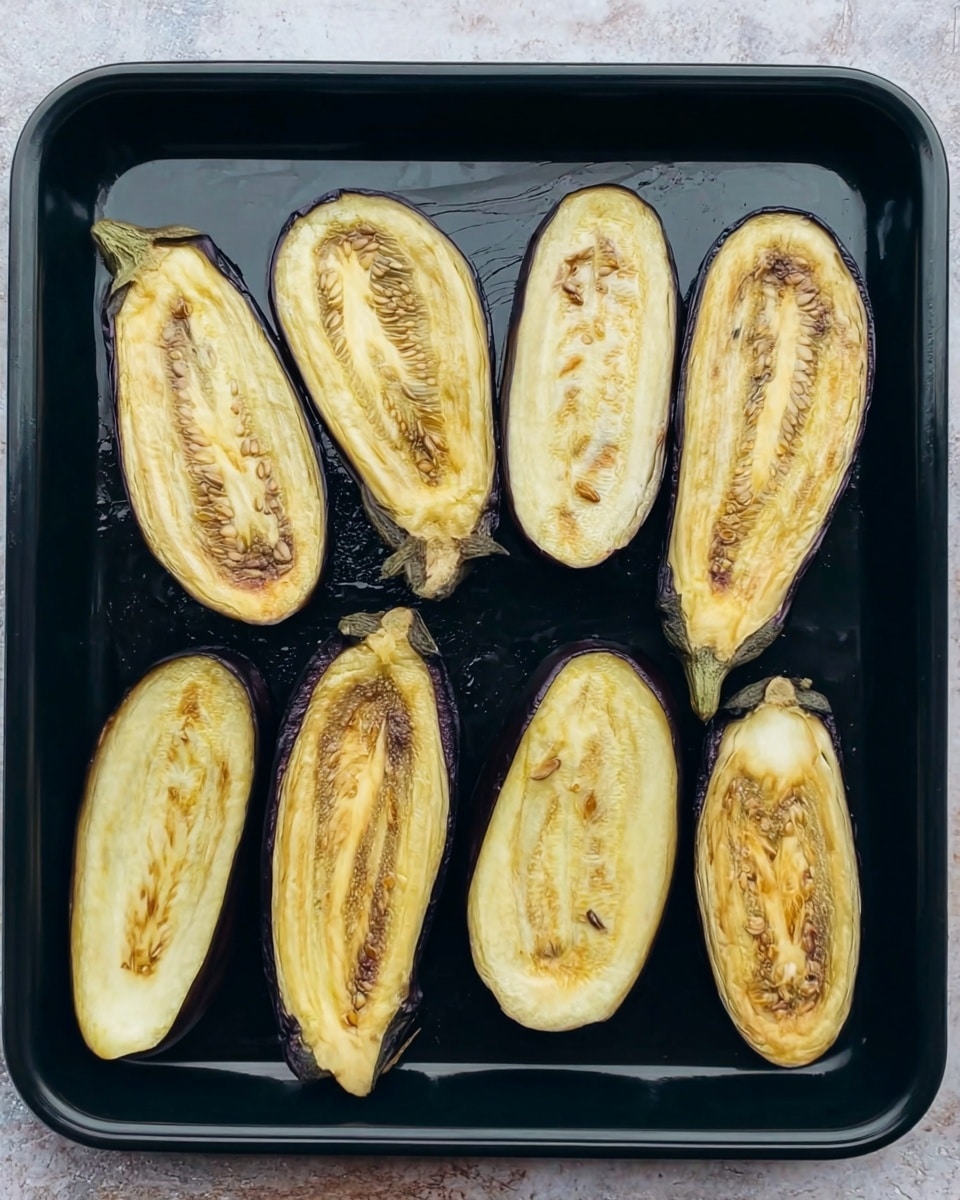 The image shows eight slices of eggplant placed on a black baking tray. Each slice has a pale yellow inside with brown seeds and some areas showing a roasted light brown edge. The skins are a dark purple color, and the slices vary in size and shape, mostly long oval or round. The tray sits on a white marbled surface with some light reflections. The eggplant slices look soft and cooked. photo taken with an iphone --ar 4:5 --v 7