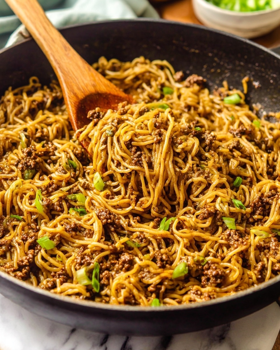The image shows a black skillet filled with cooked noodles mixed with small pieces of browned ground meat and chopped green onions. The noodles are light brown and shiny, coated with sauce, and tangled with the meat and green onions scattered throughout. There is a wooden spoon resting inside the skillet, partially lifting some of the noodles, with a white marbled surface underneath the skillet and some blurred background items. The scene is warm and inviting, focusing on the texture and color contrast between the noodles, meat, and green onions photo taken with an iphone --ar 4:5 --v 7