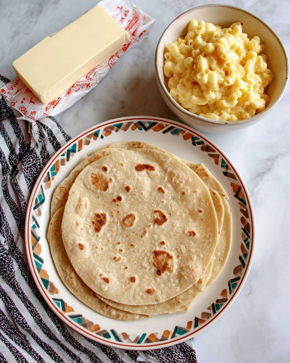 Three light brown flour tortillas with small darker spots are stacked slightly overlapping on a white plate with brown, green, blue, and tan geometric patterns around the edge, placed on a white marbled surface. Next to the plate is a stick of butter in a white wrapper with red accents, and below is a white bowl filled with creamy, yellow mac and cheese on a black and white striped cloth. Photo taken with an iphone --ar 4:5 --v 7