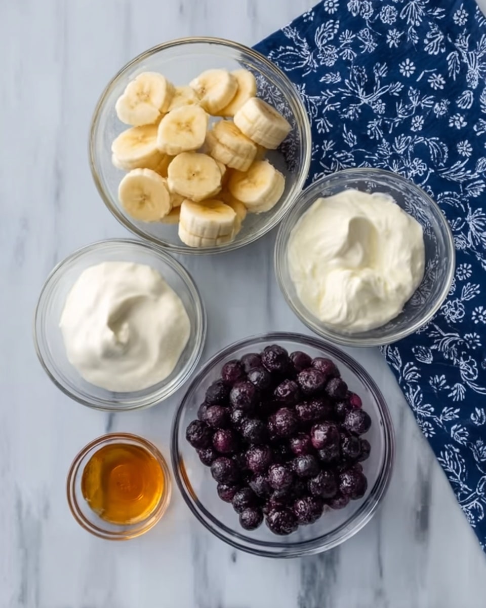 The image shows four clear glass bowls arranged on a white marbled surface with a folded dark blue cloth with white patterns on one side. The largest bowl at the bottom right is filled with small dark purple frozen berries, almost filling the bowl. Above it to the top left, a medium bowl contains small pale yellow banana slices, stacked unevenly. To the right of the banana slices, a smaller bowl holds thick white yogurt with a smooth texture. Down to the bottom left, another small bowl contains golden honey with a slight sheen and liquid texture. Above the yogurt bowl and to the top right corner, a tiny bowl has a small amount of dark amber liquid in it. Photo taken with an iphone --ar 4:5 --v 7