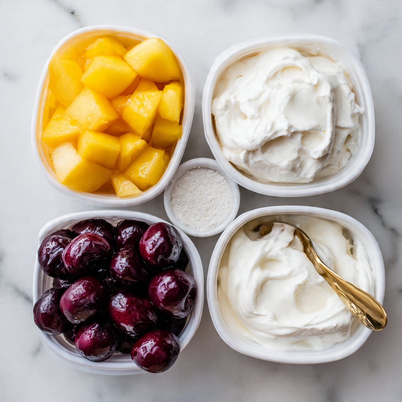 A top view of four separate white containers on a white marbled surface, arranged in a loose square. The top left container holds yellow and orange chunks of fruit with a smooth, shiny texture. Below it, the bottom left container is filled with dark red to purple whole cherries that look glossy and moist. To the right of the cherries, there is a small white bowl with a white powdery substance that looks dry and fluffy. Above it, the top right container is filled with thick, white creamy yogurt with a golden spoon standing inside, showing a smooth texture. Photo taken with an iphone --ar 4:5 --v 7