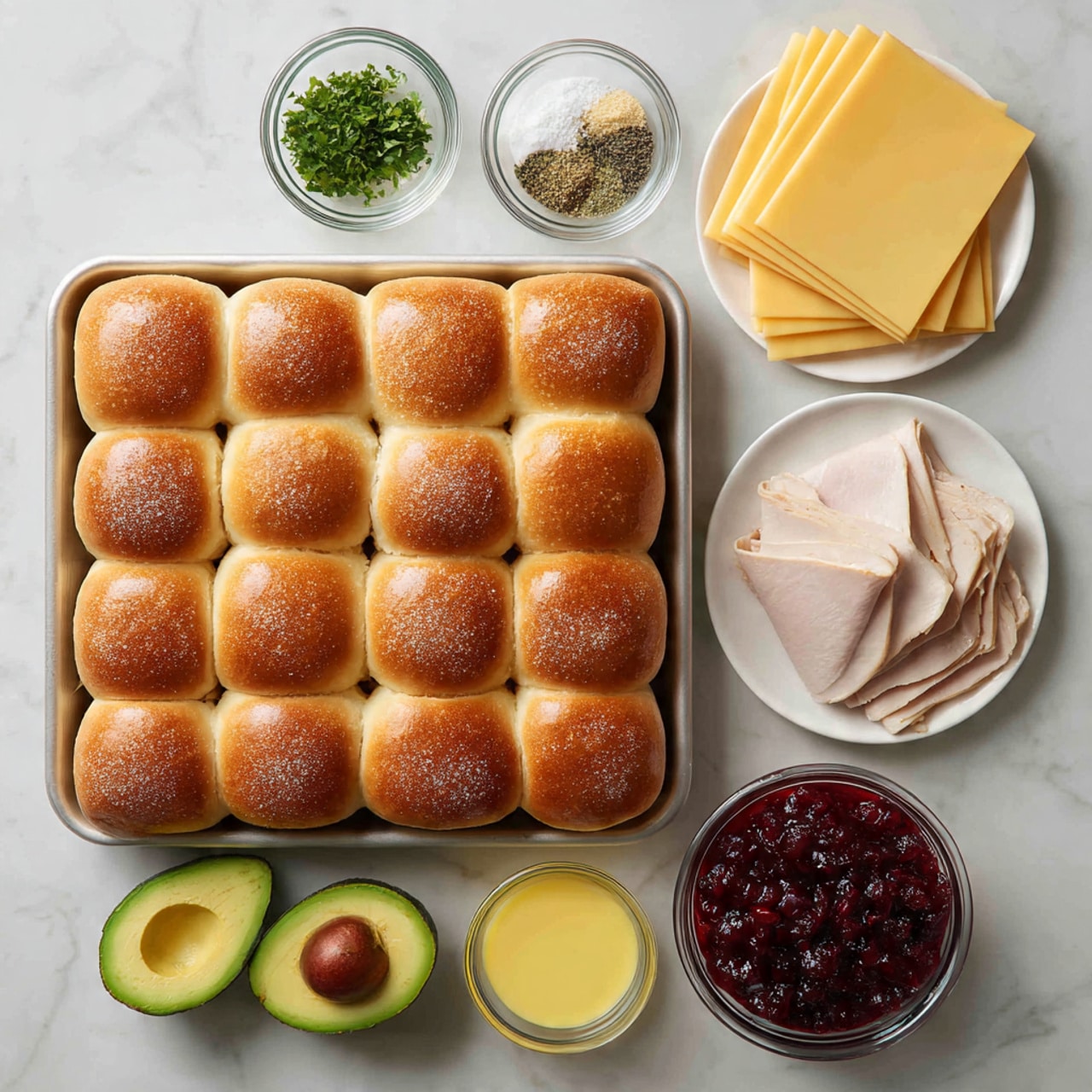 The image shows a tray with 24 soft, golden-brown slider buns arranged in a 4 by 6 grid. Above the tray, there are three small clear bowls holding chopped green herbs, coarse salt, and crushed black pepper. To the right, there is a white plate stacked with several thin, yellow slices of cheese next to a clear bowl filled with a dark red, chunky cranberry sauce. Below the tray, there is a whole avocado cut in half displaying its green smooth flesh and brown pit, a clear bowl with thin slices of light pink turkey meat, and a small clear bowl filled with bright yellow melted butter. All items are placed on a white marbled surface. photo taken with an iphone --ar 4:5 --v 7